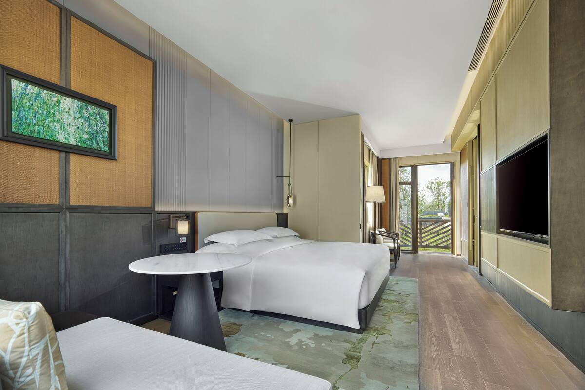 Habitación de hotel moderna con una cama grande, una mesita, un televisor y vistas al exterior.