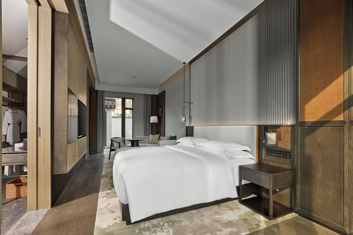 Una habitación de hotel moderna con una cama grande, una mesita de noche, un televisor y un armario.