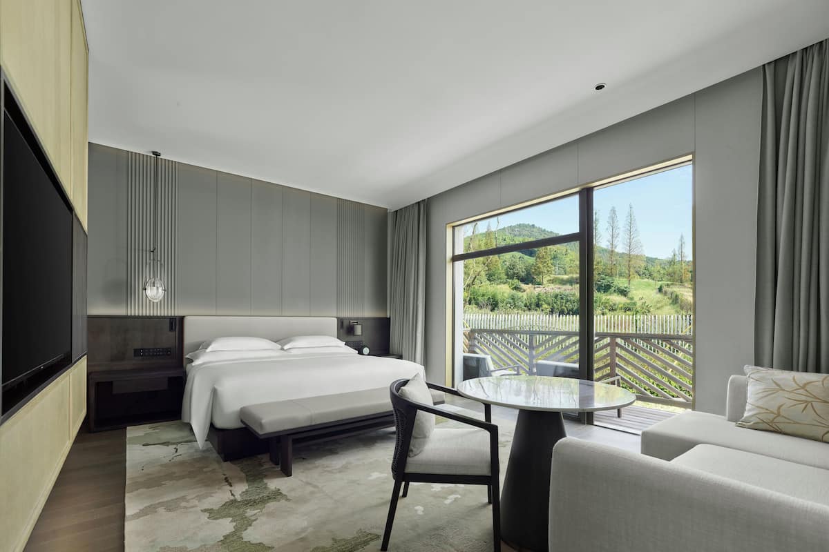 Una habitación de hotel moderna con una cama grande, un escritorio y vistas a un paisaje verde.
