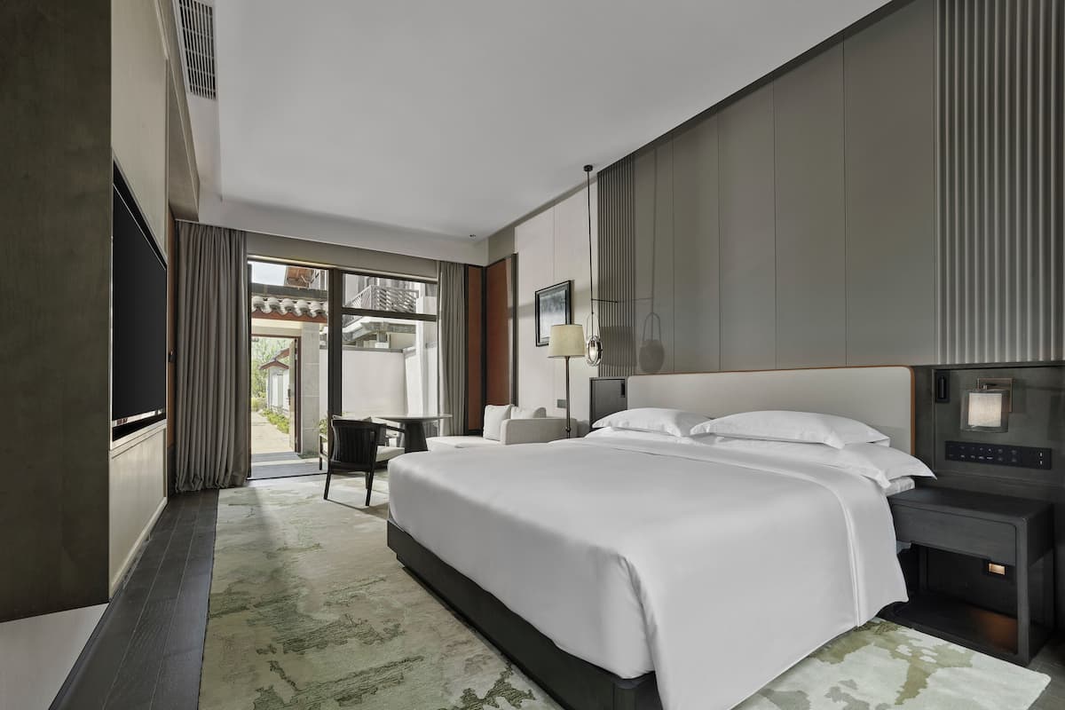 Una habitación de hotel moderna con una cama grande, un televisor de pantalla plana, un escritorio con lámpara y vistas al exterior.