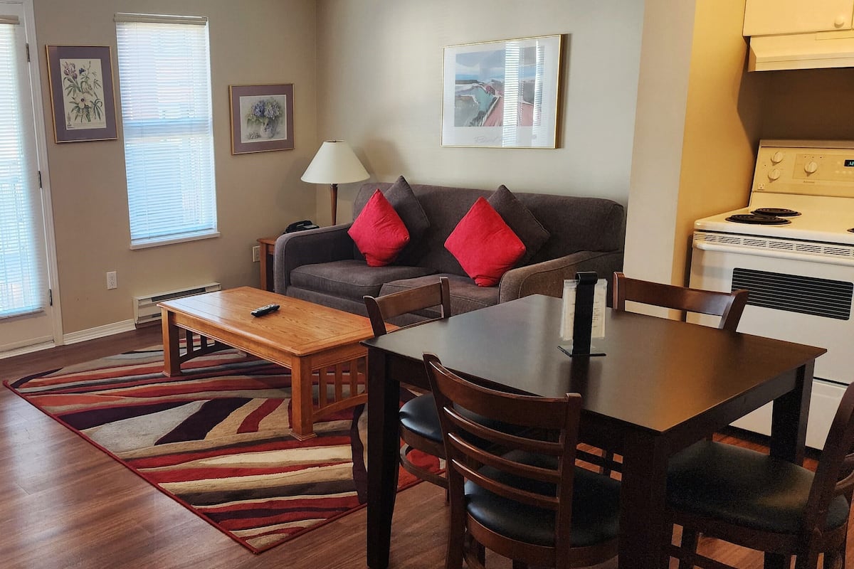 A living room with a sofa, coffee table, and dining table with chairs. There is a stove in the kitchen area.
