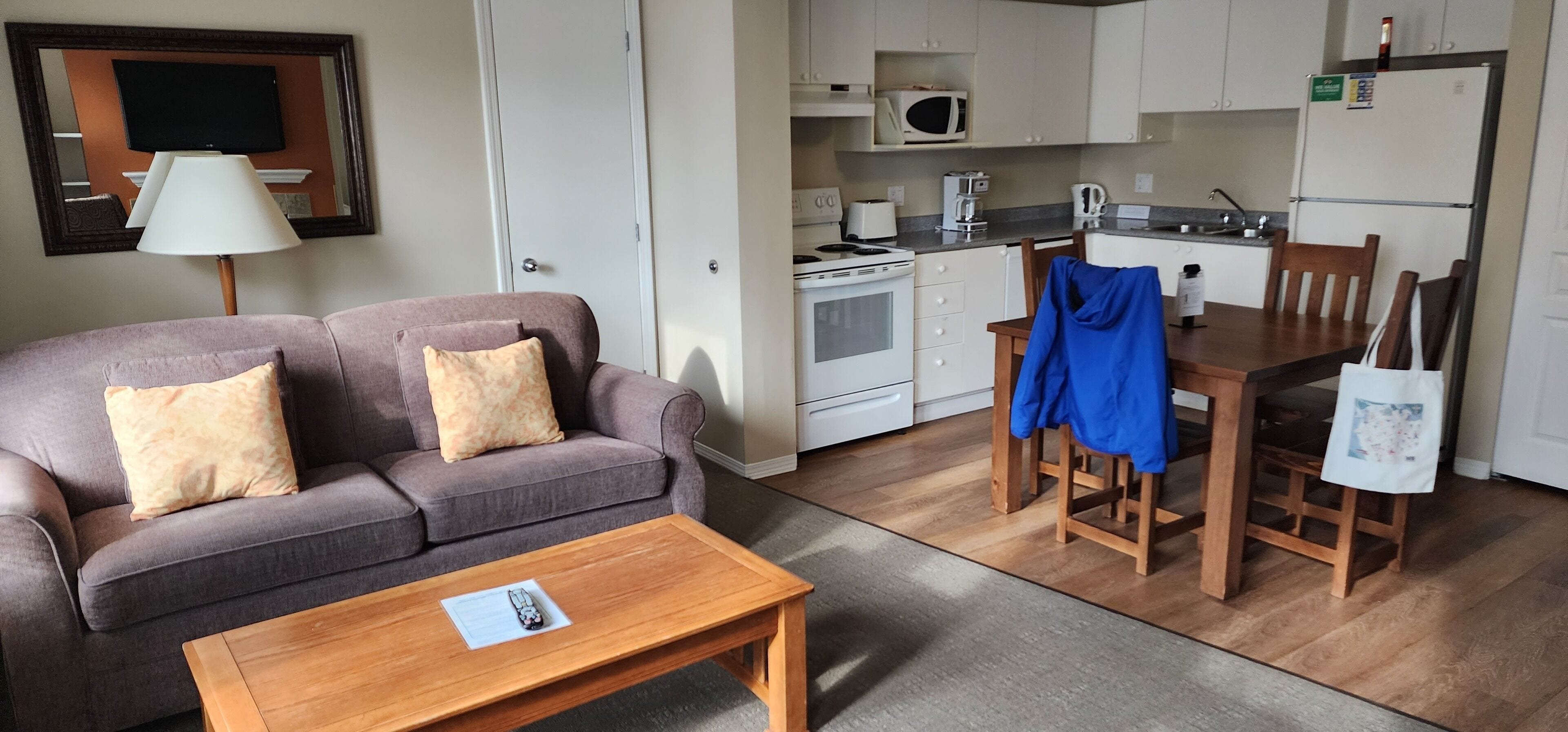 Un espacio habitable compacto con un sofá, una mesa de madera, y una cocina que incluye microondas, estufa y refrigerador.