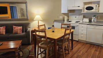 A compact living space with a sofa, a wooden dining table with chairs, a kitchen area with a stove, microwave, and dishwasher.