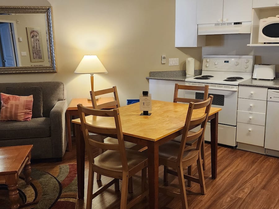 A compact living space with a sofa, a wooden dining table with chairs, a kitchen area with a stove, microwave, and dishwasher.
