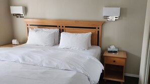 A neatly made bed with white linens, a wooden headboard, bedside tables with lamps, and a tissue box. - Times Square Suites Hotel  (Vancouver)