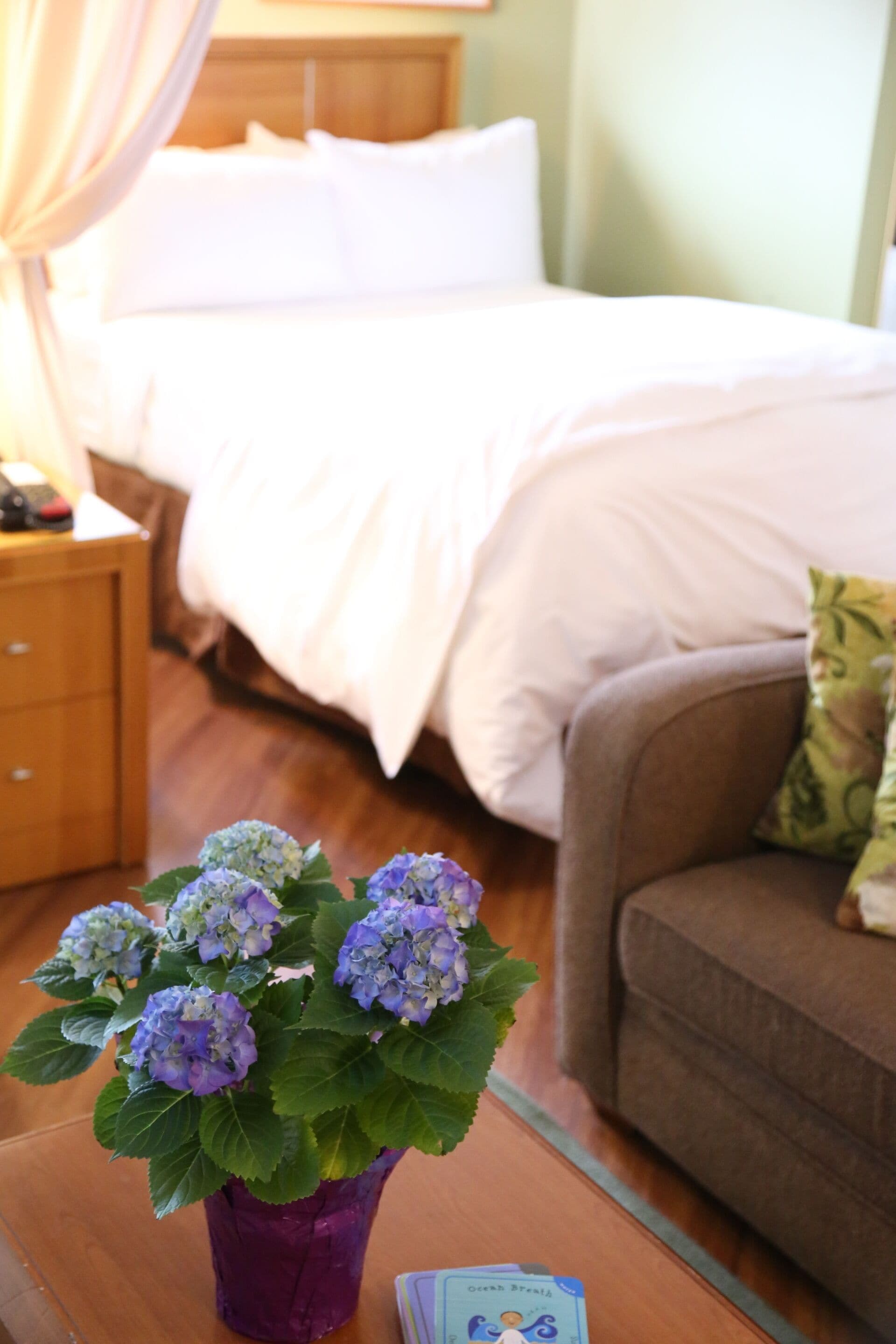 A room with a bed, a nightstand, a purple vase with flowers, and a brown couch.