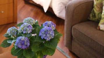 A room with a bed, a nightstand, a purple vase with flowers, and a brown couch.