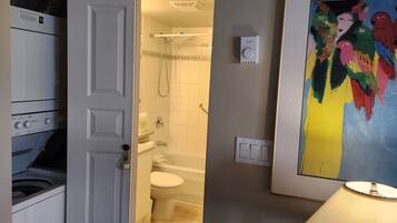Ein Badezimmer mit Waschmaschine, Toilette, Badewanne und Heizungssteuerung.