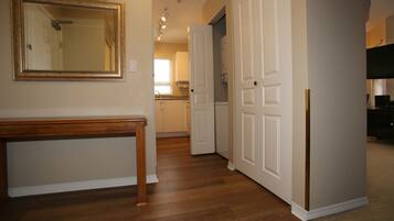A hallway with wooden flooring, a wooden bench, a mirror, and white doors leading to a kitchen area.