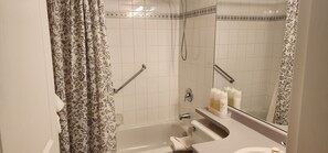 A bathroom with a bathtub, a shower with a handheld showerhead, a toilet, and a sink with toiletries. - Times Square Suites Hotel  (Vancouver)