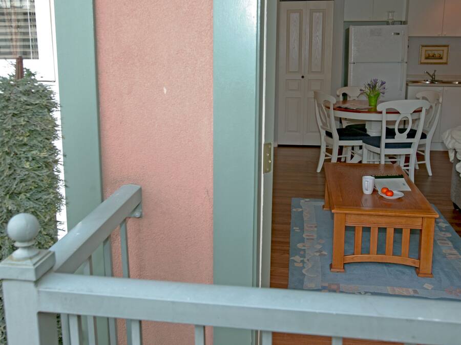 A room with a dining table, chairs, a sofa, and a kitchen area with a refrigerator and sink.