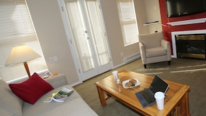 A living room with a sofa, a coffee table with a laptop and a cup, a fireplace, and a TV mounted on the wall. - Times Square Suites Hotel  (Vancouver)