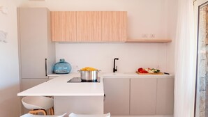 Una cocina compacta con una encimera blanca, dos taburetes de bar blancos, un mueble de madera, un dispensador de agua azul y una olla en la estufa.