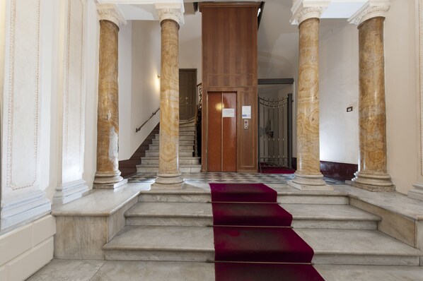 A grand staircase with marble columns and a red carpet leading to a wooden door.
