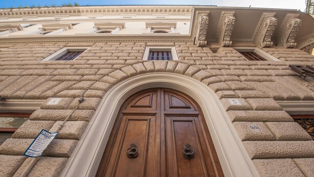 A large, ornate wooden door with a decorative architrave, flanked by stone blocks and columns, leading to a building with classical architectural elements. - Monti Deluxe - Terrace Spectacular View (Rome)