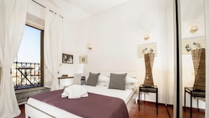 A bedroom with a bed, a bedside table, a chair, a window with curtains, and artwork on the walls. - Monti Deluxe - Terrace Spectacular View (Rome)