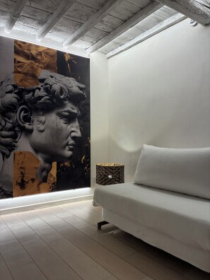 Une pièce moderne avec un canapé blanc, une grande fresque murale et un plafond avec des poutres apparentes.