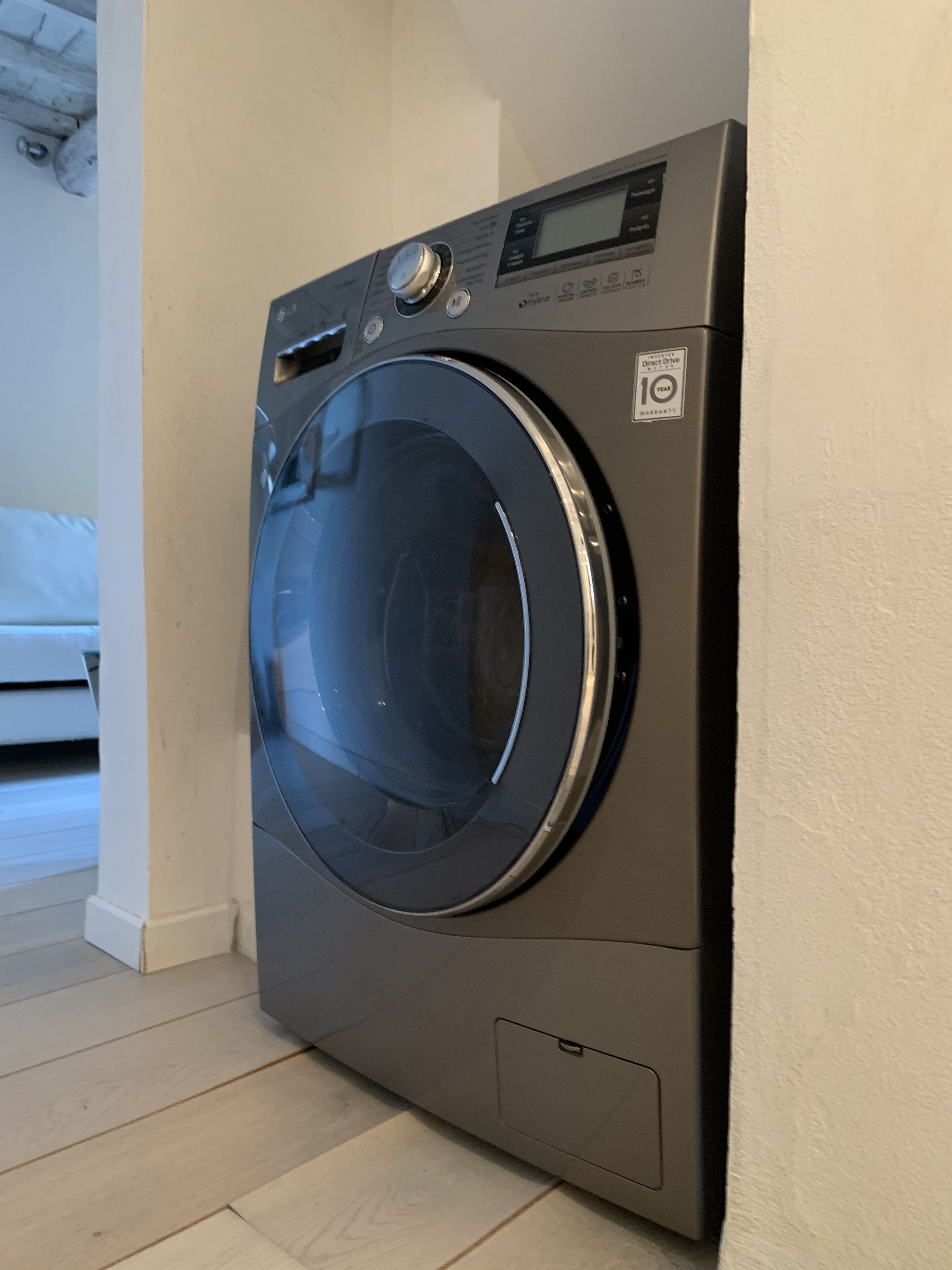 Una lavadora de carga frontal en una habitación con suelo de madera y pared blanca.