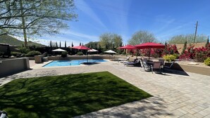 Un jardin avec une piscine, des chaises longues et des parasols rouges.