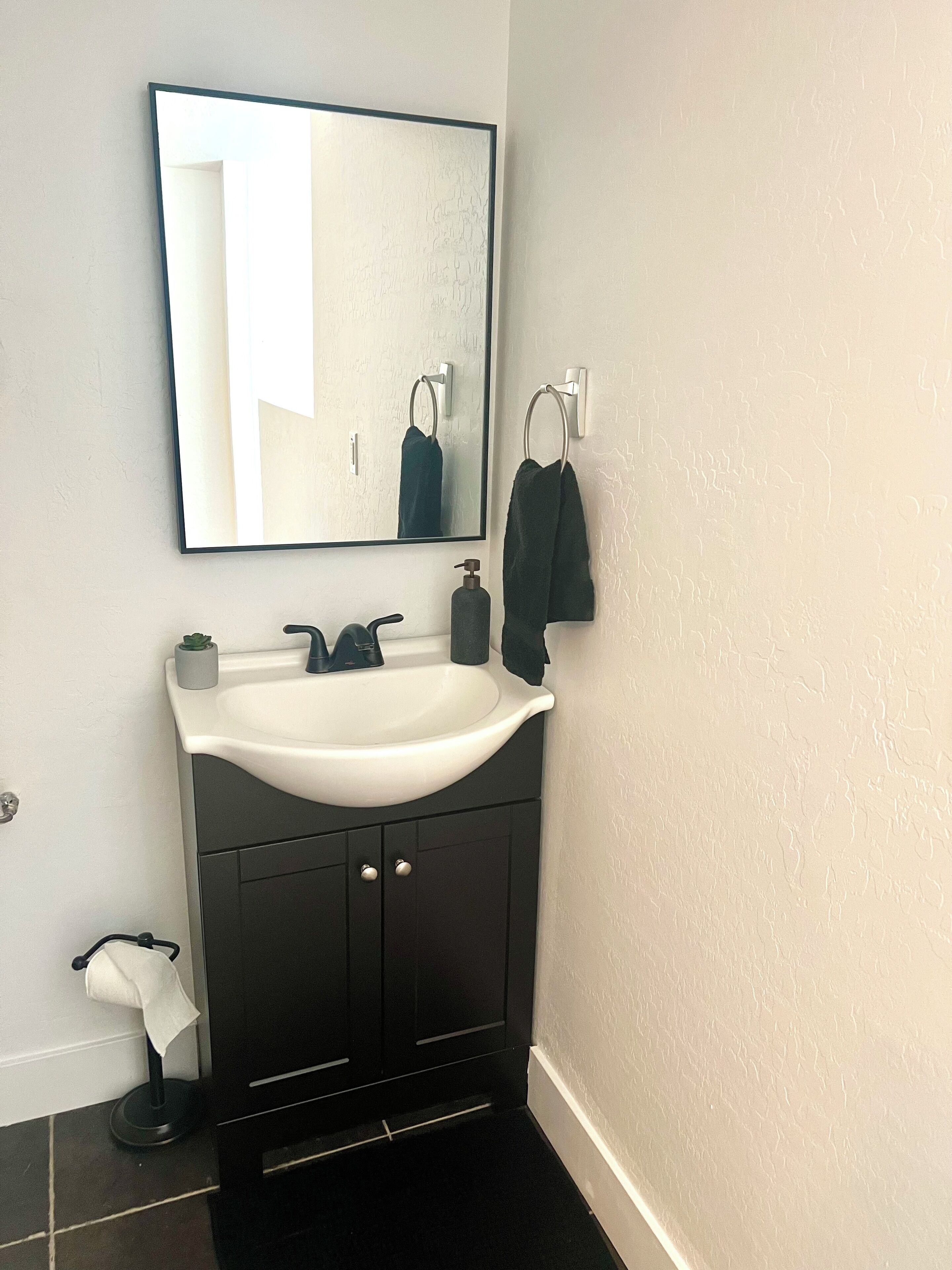 Une salle de bain avec un lavabo blanc, un meuble noir et un grand miroir.