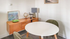 En matplats med ett runt bord, två stolar, ett träskåp, en jordglob, en lampa och en inramad tavla på väggen.
