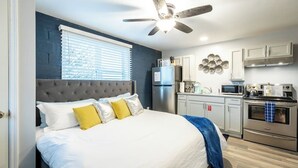 A bedroom with a large bed, a ceiling fan, a kitchen with modern appliances, and a window with blinds. - Suite 212 - Exhale at Rock Spring Resort (Rock Spring)