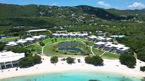 Vue aérienne d’un complexe hôtelier comprenant plusieurs bâtiments, une plage et un lagon aux eaux bleu cristallin.