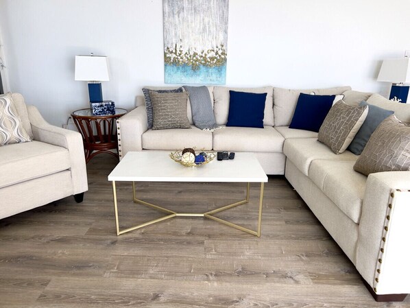 A living room with a beige sofa, a white coffee table with gold legs, and a blue abstract painting on the wall.