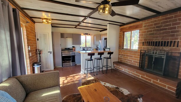 A spacious living area with a wooden ceiling, a fireplace, a kitchen in the background, and a sofa.
