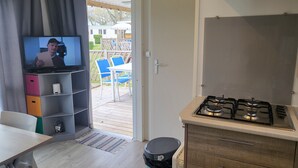 Una cocina compacta con estufa a gas, un televisor en un estante, y vista a un patio exterior con sillas y una mesa.