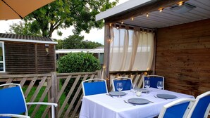 Un patio al aire libre con una mesa dispuesta para cuatro personas, rodeado de sillas azules, bajo una pérgola de madera con luces colgantes.