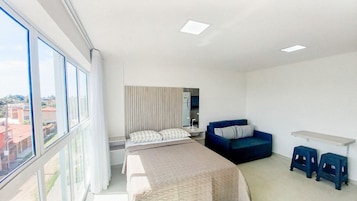 Una habitación de hotel moderna con un ventanal grande, una cama, un sofá, un escritorio y un espejo.