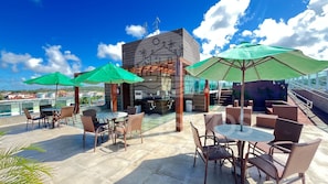 A rooftop terrace with outdoor seating, a barbecue area, and a view of the city. - Flats no Beach Way - Praia dos Carneiros (Tamandaré)