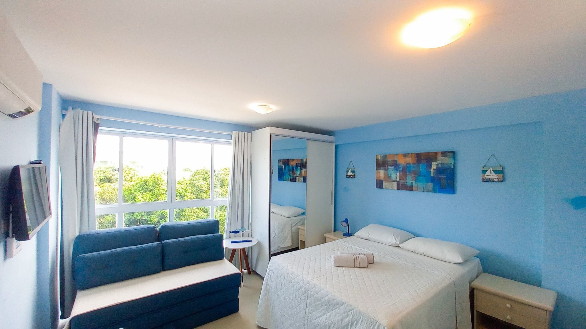 A bedroom with a bed, a sofa, a bedside table, a mirror, and a window with curtains.