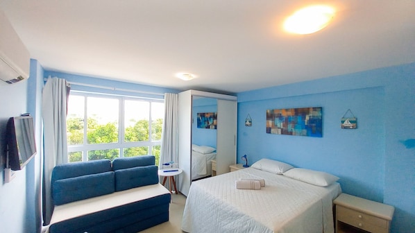 Quarto com cama, sofá, mesa de cabeceira, espelho e janela com cortinas.