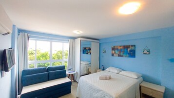 Un dormitorio con cama, sofá, mesita de noche, espejo y ventana con cortinas.