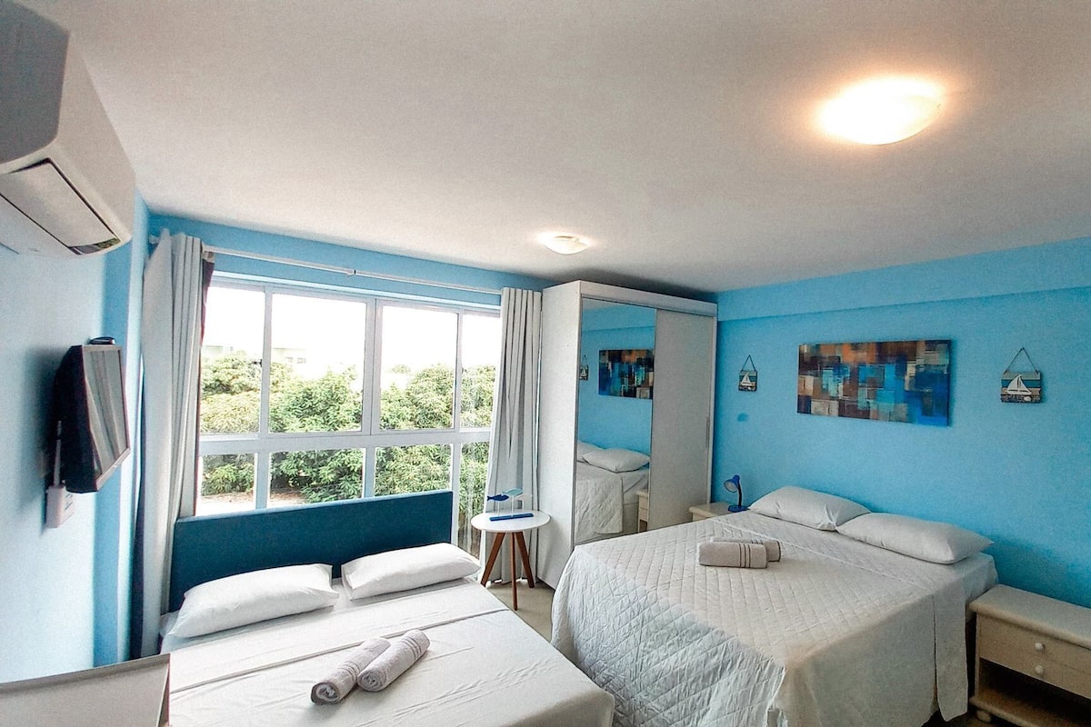 A hotel room with two beds, a small table, a mirror, and a window with curtains.