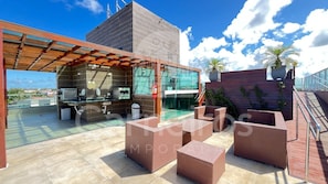Um terraço no telhado com cozinha ao ar livre, espaço para sentar e vista da cidade.