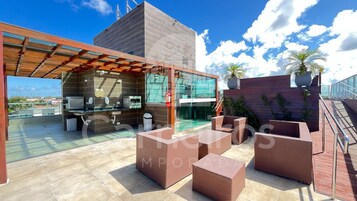 Una terraza en la azotea con cocina al aire libre, asientos y vistas de la ciudad.