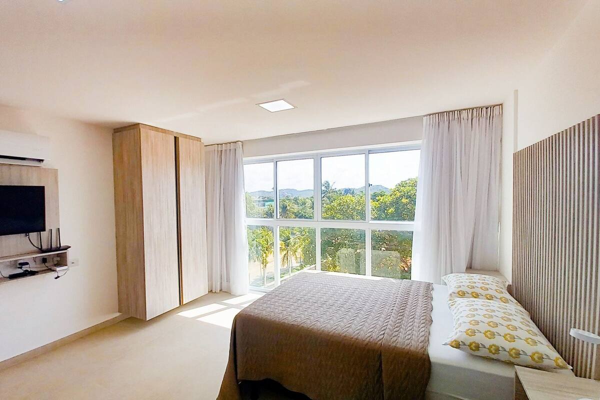 A bedroom with a bed, a TV mounted on the wall, and a large window with curtains.