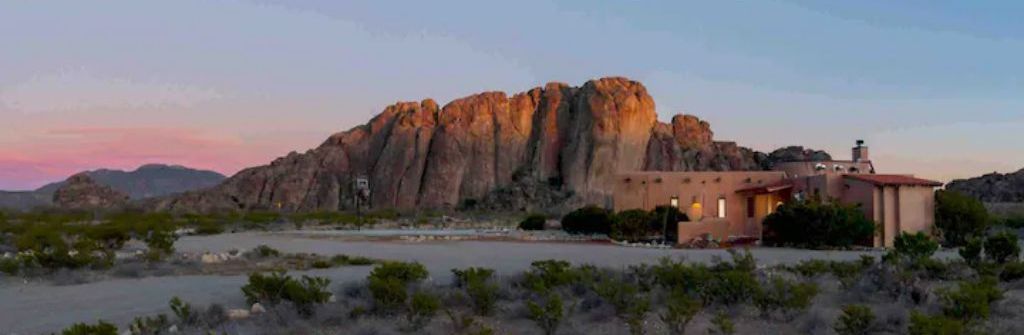 A desert landscape with a prominent rock formation and a building with a red roof.