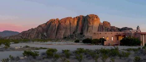 A desert landscape with a prominent rock formation and a building with a red roof.