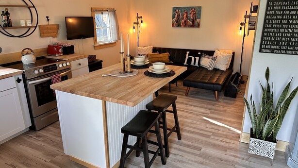 A modern kitchen with a central island, wooden flooring, and a dining area with a sofa and a painting.