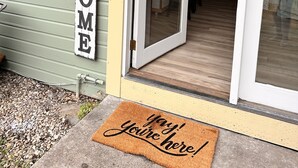 A house with a 'WELCOME' sign, a sliding glass door, and a doormat with 'Yay! You're here!' written on it.