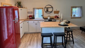 A kitchen with a red refrigerator, wooden cabinets, a coffee bar, a stove, and a dining area with stools.