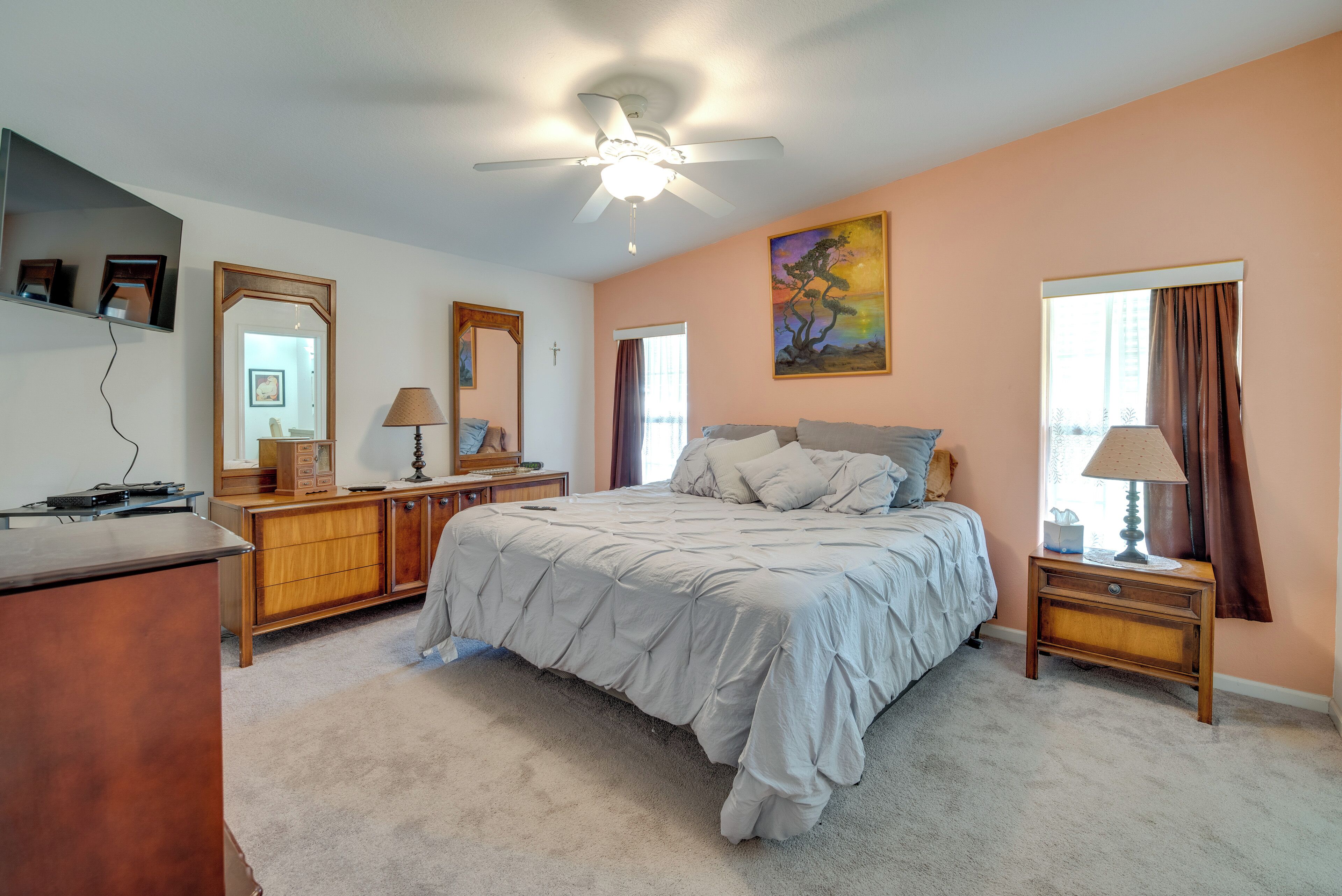 Une chambre à coucher comprenant un lit, un ventilateur de plafond, une commode, une table de chevet avec une lampe et un tableau accroché au mur.