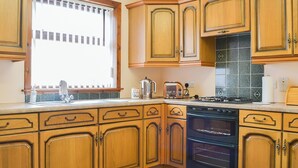 A kitchen with wooden cabinets, a dishwasher, a stove, and a window with blinds. - 3 bedroom accommodation in Portknockie (Portknockie)