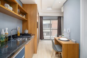 A modern kitchen with a sink, stove, and wooden shelves, a dining area with a table and chairs, and a view through a large window.