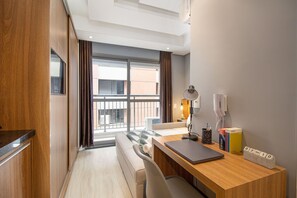 Une chambre d’hôtel avec un bureau en bois, un ordinateur portable, une lampe, une bibliothèque et une vue sur l’extérieur.