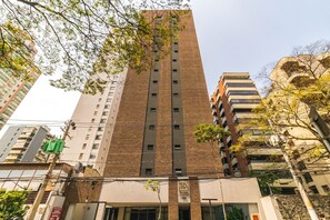 A tall brick building with multiple windows and balconies, surrounded by other buildings and trees.